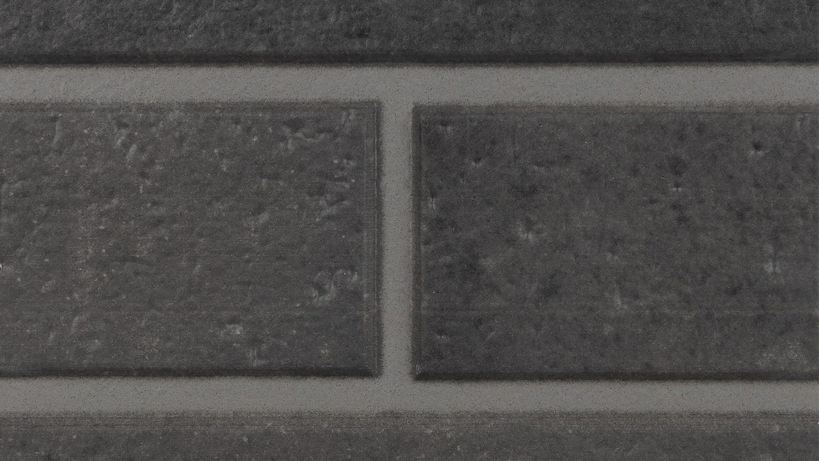 A close-up shot of a dark gray tile wall, showcasing four tiles arranged in a rectangular pattern. The tiles have a slightly rough texture and are separated by thin grouting lines. The whole arrangement displays uniformity and a modern aesthetic.