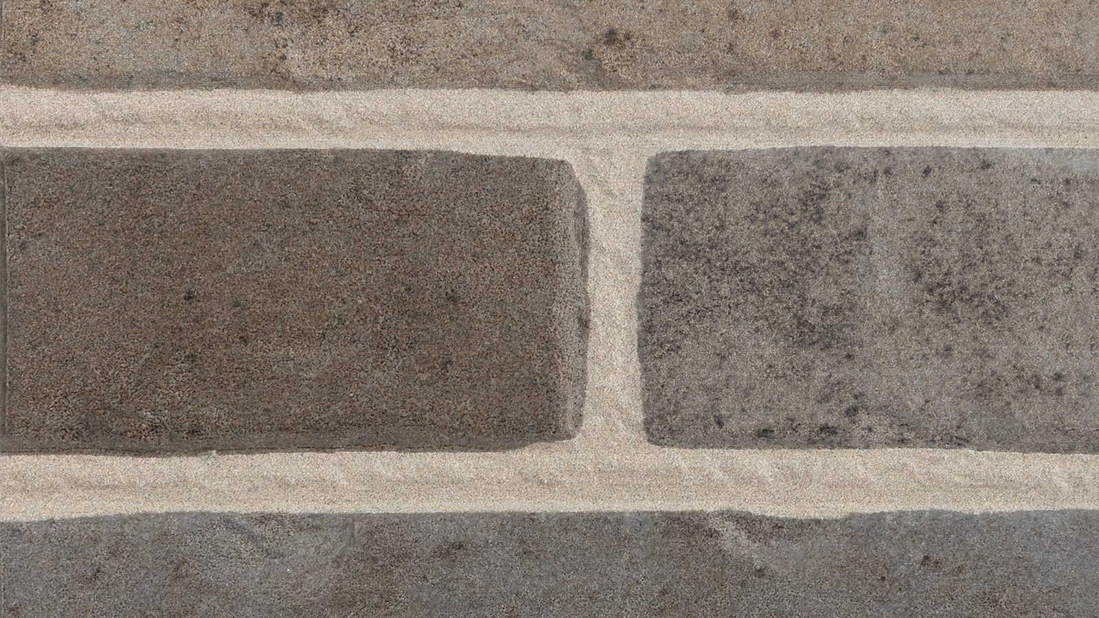 Close-up view of a brick wall with large rectangular stones placed horizontally. The stones have a rough texture with varying shades of grey and brown, separated by light-colored grout lines creating a grid pattern.
